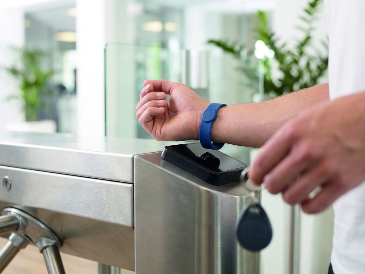 Pulsera RFID de silicona en un torno de acceso de gimnasio y llavero RFID en la mano